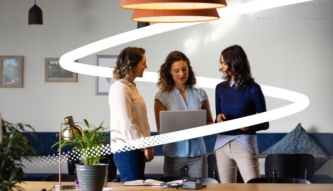 three female colleagues discuss around a laptop image for Valamis guide to AI in corporate training