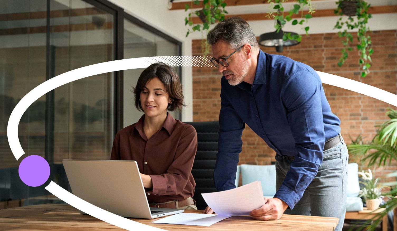 Two professionals reviewing work together on a laptop in a modern office setting.