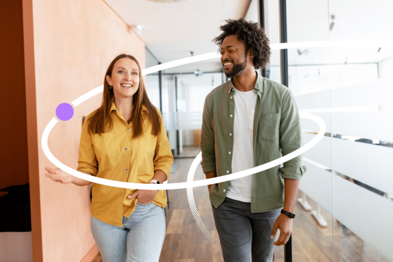 Two colleagues talking and smiling as they walk together through a bright, modern office hallway.
